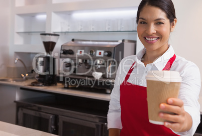 Happy young barista offering cup of coffee to go smiling at came