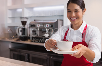 Happy young barista offering cup of coffee smiling at camera