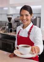 Pretty young barista offering cup of coffee smiling at camera