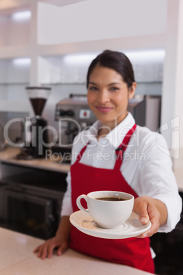 Pretty barista offering cup of coffee smiling at camera