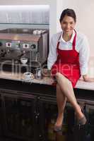 Pretty barista smiling at camera sitting on counter