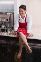 Pretty barista sitting on counter and smiling