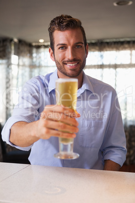 Happy businessman raising glass of beer to camera after work