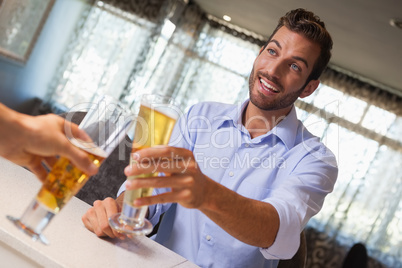Smiling businessman clinking glass of beer with bartender