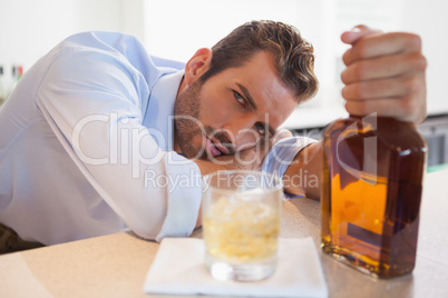 Drunk businessman clutching whiskey bottle looking at camera