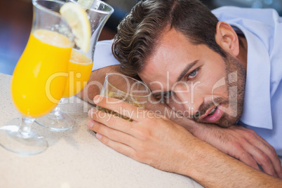 Drunk businessman slumped on bar beside cocktail