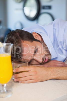 Drunk businessman asleep on bar beside cocktail