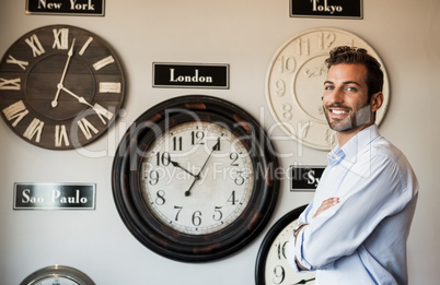 Happy businessman standing beside wall of international clocks