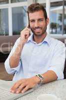 Smiling businessman talking on phone using his laptop