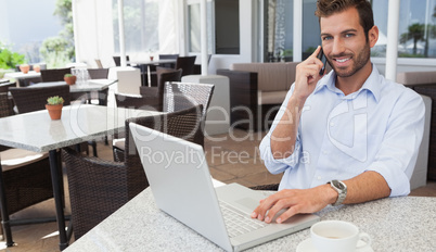 Cheerful businessman talking on phone using his laptop