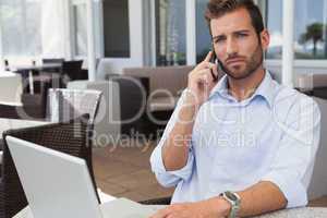 Frowning businessman talking on phone using his laptop