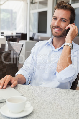 Smiling young businessman talking on phone using his laptop