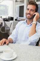 Smiling young businessman talking on phone using his laptop