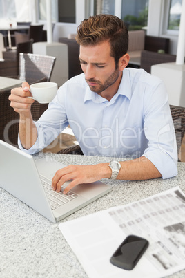Frowning young businessman using his laptop holding coffee cup