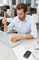 Frowning young businessman using his laptop holding coffee cup