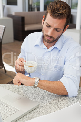 Frowning young businessman checking time holding coffee cup