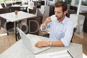 Frowning young businessman working at laptop drinking coffee