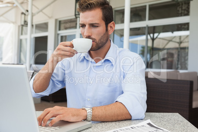 Serious young businessman working at laptop drinking coffee