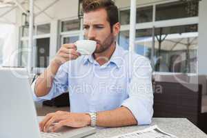 Serious young businessman working at laptop drinking coffee