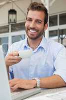 Happy young businessman working at laptop drinking coffee