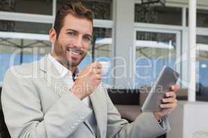 Cheerful young businessman working on tablet drinking espresso