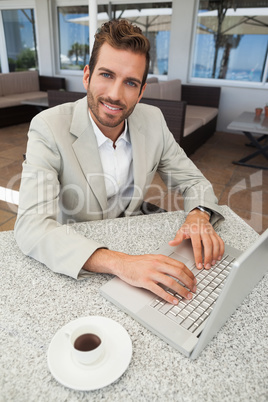 Smiling businessman working with his laptop at table having coff