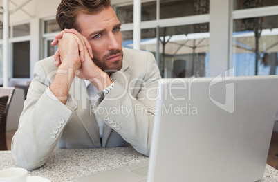 Frowning businessman looking at his laptop at table having coffe