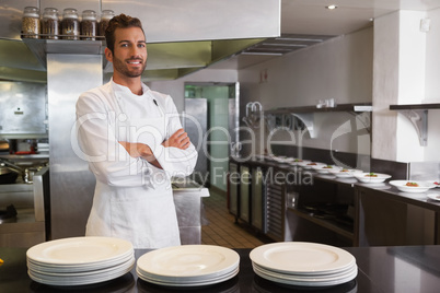 Smiling young chef standing with arms crossed behind counter