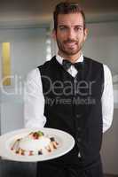 Smiling waiter showing plate of dessert to camera