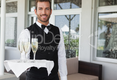 Handsome smiling waiter holding tray of champagne