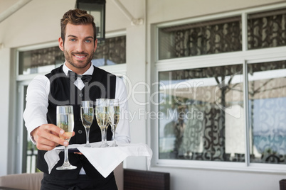 Handsome smiling waiter offering flute of champagne