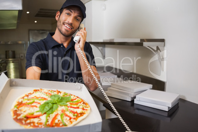 Smiling pizza delivery man taking an order over the phone showin