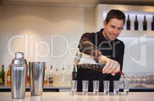 Happy bartender pouring cocktail into shot glasses