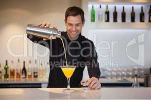 Smiling bartender pouring yellow cocktail into glass