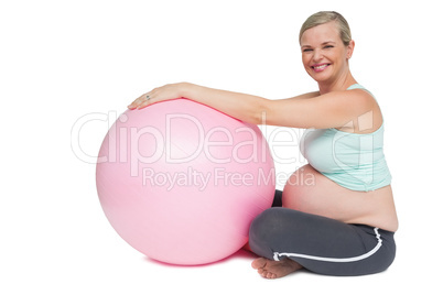 Smiling pregnant woman leaning against pink exercise ball