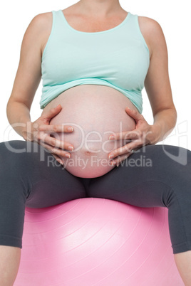 Pregnant woman sitting on pink exercise ball holding her belly