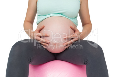 Pregnant woman sitting on pink exercise ball holding her bump