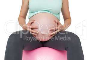 Pregnant woman sitting on pink exercise ball holding her bump
