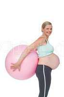 Happy pregnant woman holding pink exercise ball behind her back