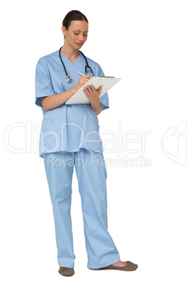 Smiling pretty nurse in scrubs writing on clipboard