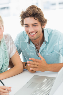 Closeup of a smiling young man with laptop at desk