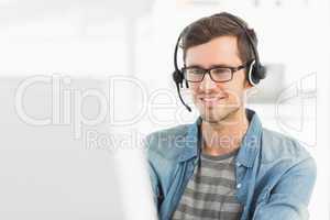 Smiling casual young man with headset using computer