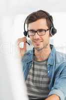 Smiling casual young man with headset using computer