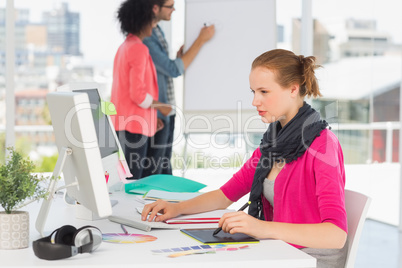 Female artist using graphic tablet with colleagues at office