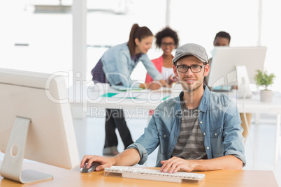 Casual male artist using computer with colleagues in background