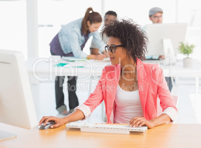 Female artist using computer with colleagues in background at of