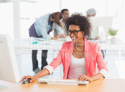 Female artist using computer with colleagues in background at of