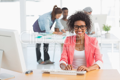 Female artist using computer with colleagues in background at of