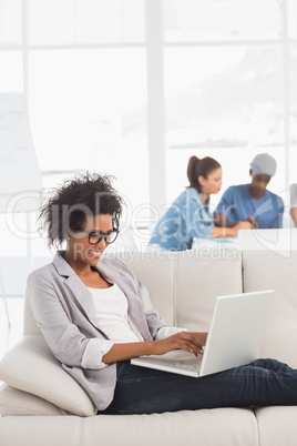 Woman using laptop with colleagues in background at creative off