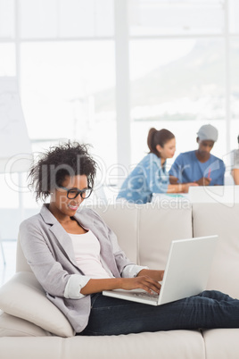 Woman using laptop with colleagues in background at creative off